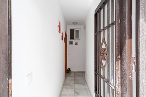 Un couloir étroit aux murs blancs, doté d’un sol carrelé et d’une porte ornée d’un portail en métal décoratif.