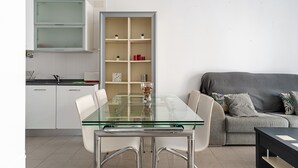 Una cocina moderna con armarios blancos, una mesa de comedor de vidrio y un sofá gris.