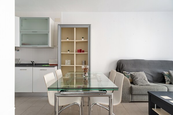 Una cocina moderna con armarios blancos, una mesa de comedor de vidrio y un sofá gris.