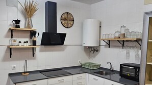 Una cocina moderna con armarios blancos, encimera negra, una mesa de comedor de vidrio y un reloj en la pared.