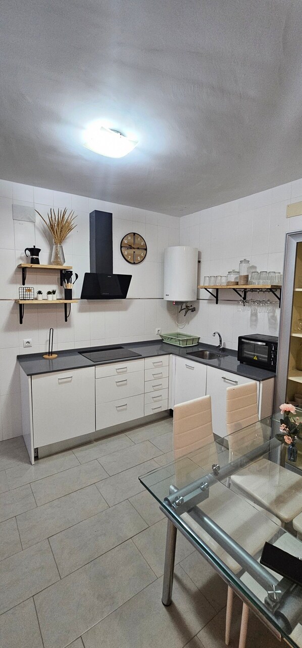 Une cuisine moderne avec des meubles blancs, un plan de travail noir, une table à manger en verre et une horloge au mur.