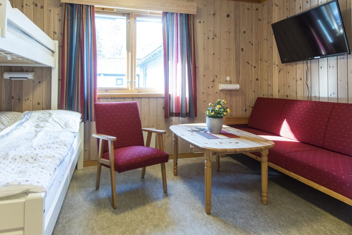A room with bunk beds, a red sofa, a wooden table, and a TV mounted on the wall.