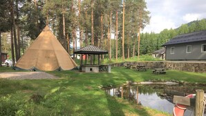 A campsite with a tent, picnic tables, a gazebo, a small pond, and a wooden deck with a lifebuoy. - Torpomoen (Al)