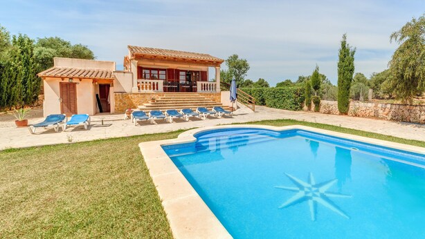 Una villa junto a la piscina con tumbonas y un pequeño edificio con balcón.