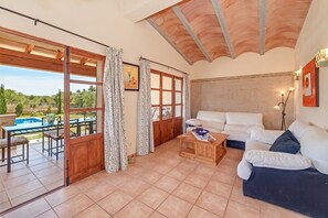Amplia sala de estar con sofá, una mesa de centro de madera y vistas a una piscina y zonas verdes.