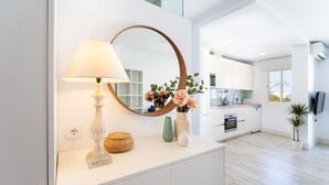 Une cuisine moderne avec des meubles blancs, un miroir rond, une lampe et un vase de fleurs posé sur un plan de travail blanc.