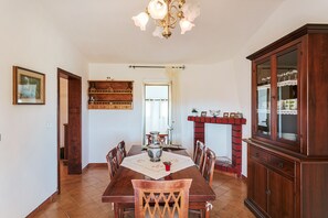 A dining room with a wooden table, chairs, a chandelier, a fireplace, and a cabinet.