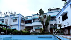 A hotel with a swimming pool, multiple balconies, and a tropical garden.