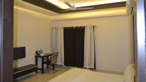 A hotel room with a bed, a desk with a chair, a flat-screen TV, and a ceiling fan.