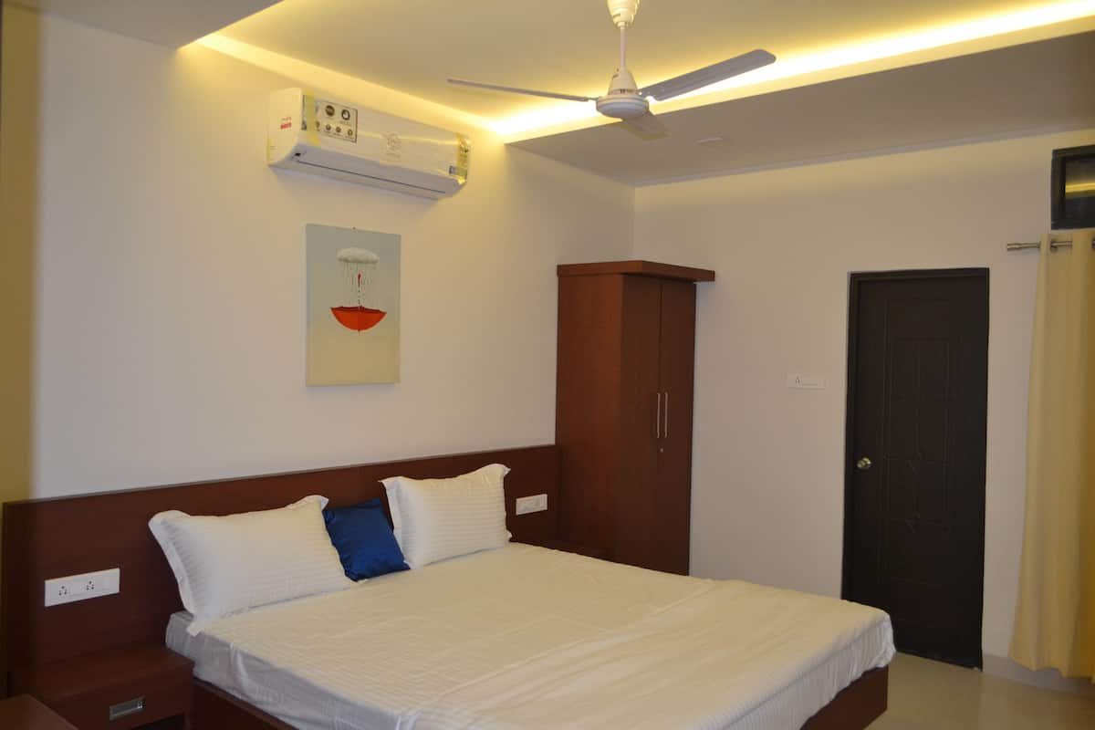 Una habitación de hotel con cama, armario, aire acondicionado, ventilador de techo y una puerta.