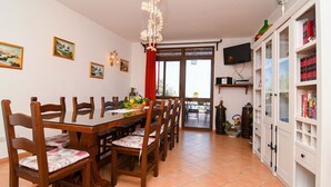 Un comedor con una mesa y sillas de madera, un televisor montado en la pared y una estantería llena de libros.