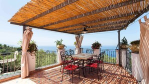 Un patio techado al aire libre con una mesa y sillas, plantas en macetas y vistas al mar.