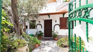Un patio con un sendero de piedra que lleva a una puerta, rodeado de plantas en macetas y un árbol.