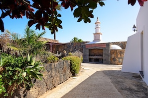 Un patio con un muro de piedra, un edificio de fachada blanca y una torre.