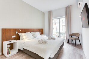 A hotel room with a bed, bedside tables, a TV, a chair, and a window with curtains.