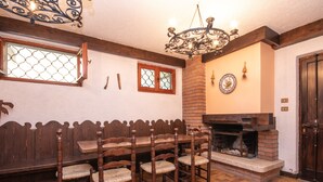 Een eetgedeelte met een houten bank, stoelen, een open haard en een kroonluchter.