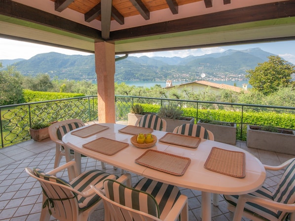 An outdoor terrace with a table and chairs, a view of mountains and a lake, and a railing.