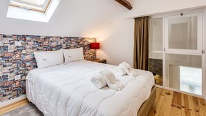 Quarto com cama, claraboia, parede com colagem de fotos, luminária vermelha e janela com cortinas.