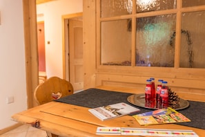 Une table en bois avec un set de table noir, une pomme de pin et des bouteilles rouges.
