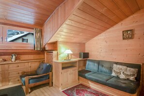 A wooden cabin interior with a sofa, chair, wooden cabinets, a window, and a lamp.