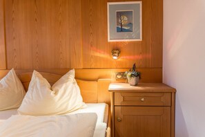 A wooden room with a bed, a nightstand with a radio, and a framed picture on the wall.