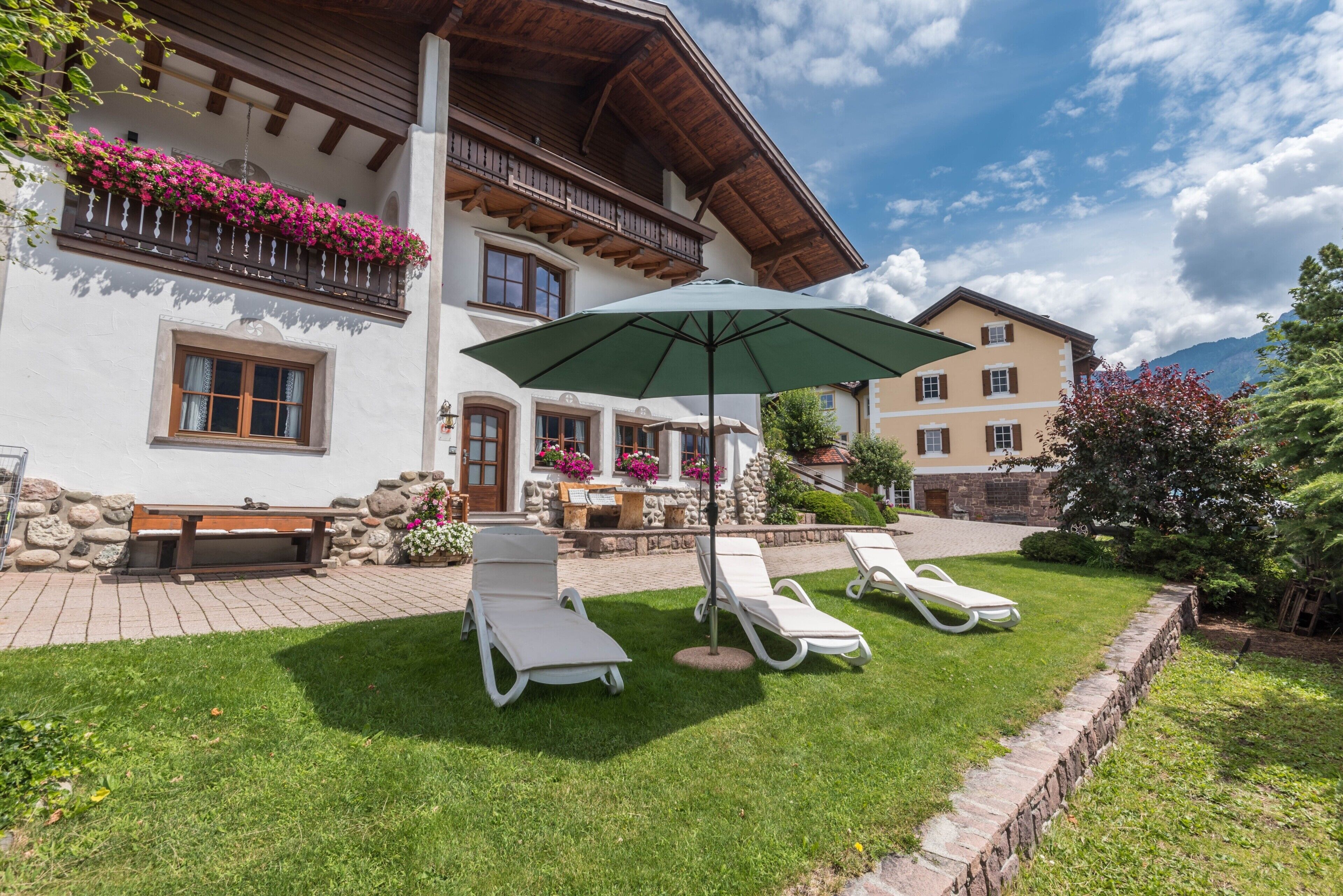 Un hôtel doté d’un balcon fleuri, d’une terrasse avec des chaises longues et une table, et offrant une vue sur la montagne.