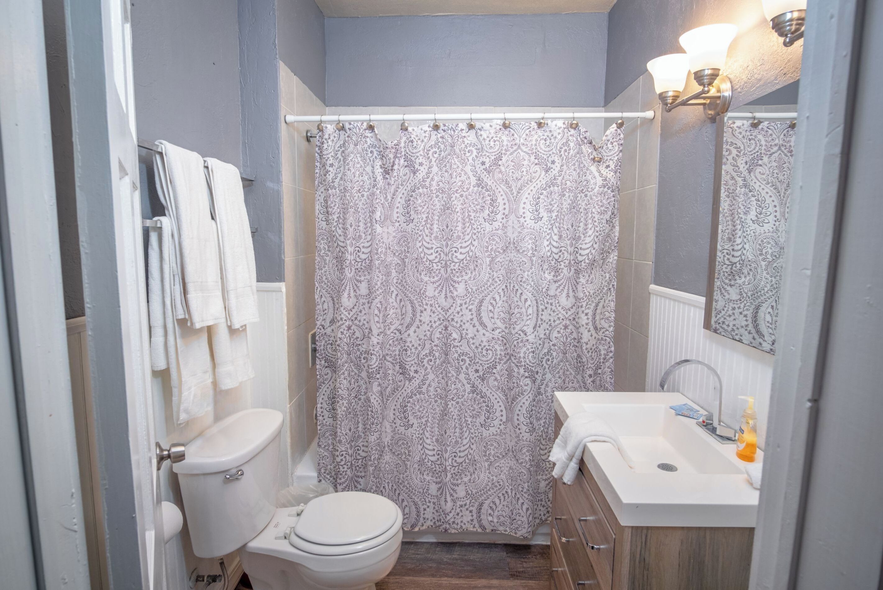 Un bagno con il water, tenda da doccia, lavandino e specchio.