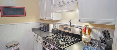A kitchen with white cabinets, a gas stove, a toaster, and a trash can.