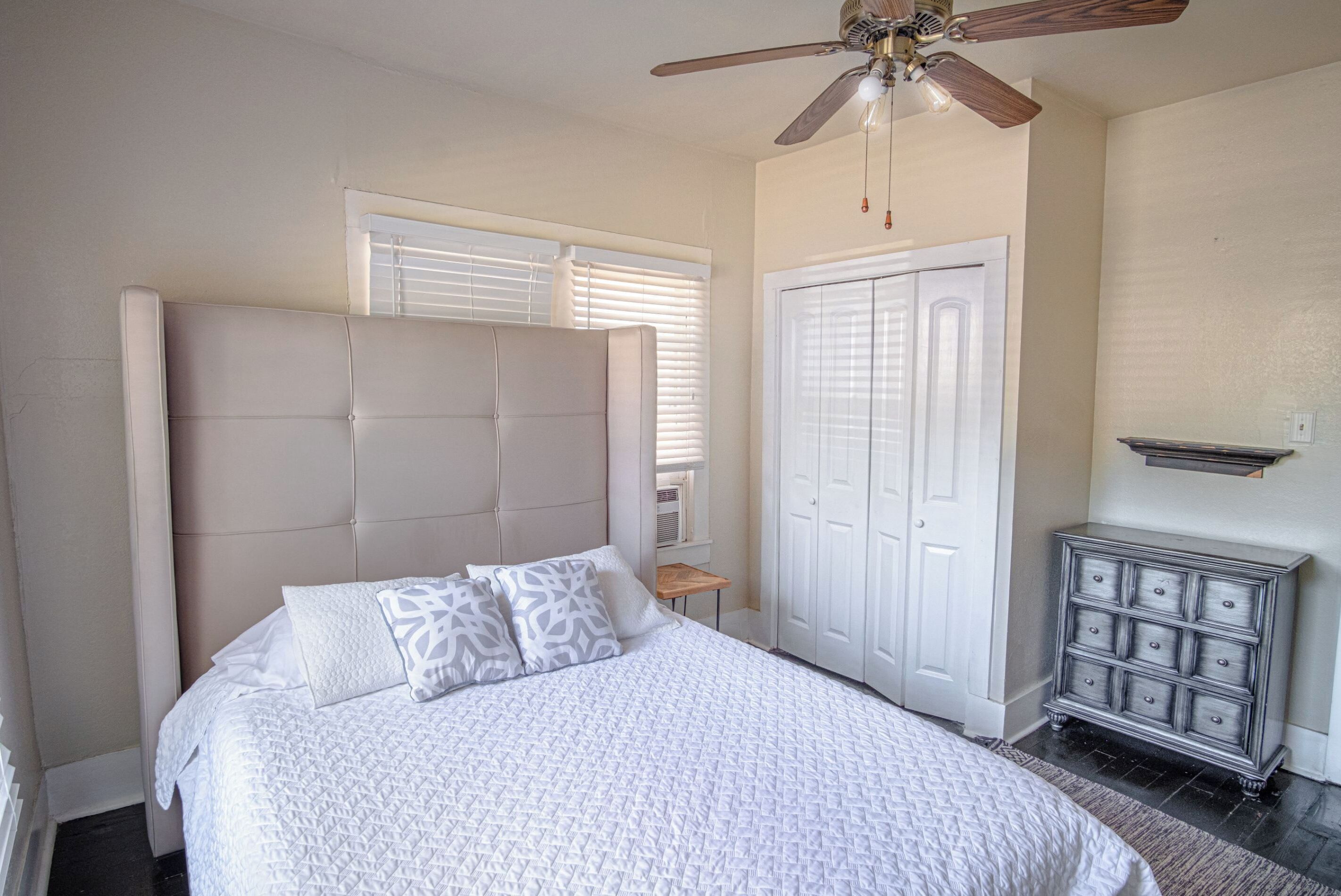 A bedroom with a large bed, a ceiling fan, a wardrobe, and a small table.