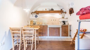 Una cocina con armarios de madera, una mesa de comedor con sillas y una cama litera con una colcha roja.