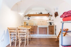 A kitchen with wooden cabinets, a dining table with chairs, and a bunk bed with a red blanket.