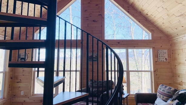 L ’intérieur d’une cabane dotée d’un escalier en colimaçon, de grandes fenêtres et d’un coin salon confortable.