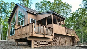 Une cabane en bois à deux étages, dotée de grandes fenêtres, d’un balcon et d’une véranda couverte.