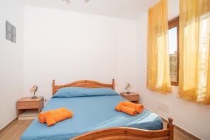 A bedroom with a wooden bed, two nightstands, a window with yellow curtains, and a wall-mounted light fixture.