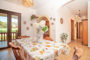 A dining area with a table set for four, a vase with flowers, and a view through an open door.