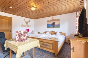 Una habitación con techo de madera, cama con ropa de cama floral, televisor y un cuadro con ciervo y vaca.