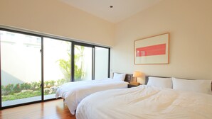A hotel room with two beds, a large sliding glass door leading to a garden, and a framed picture on the wall. - Villa Tono's Ishigakijima (Ishigaki)