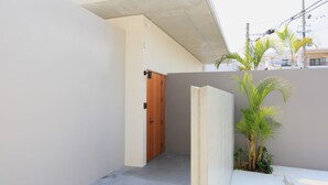 A narrow hallway with a wooden door, a concrete ceiling, and a small palm tree. - Villa Tono's Ishigakijima (Ishigaki)