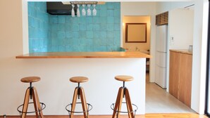 A kitchen with a blue tiled backsplash, wooden bar counter, and three wooden stools. - Villa Tono's Ishigakijima (Ishigaki)