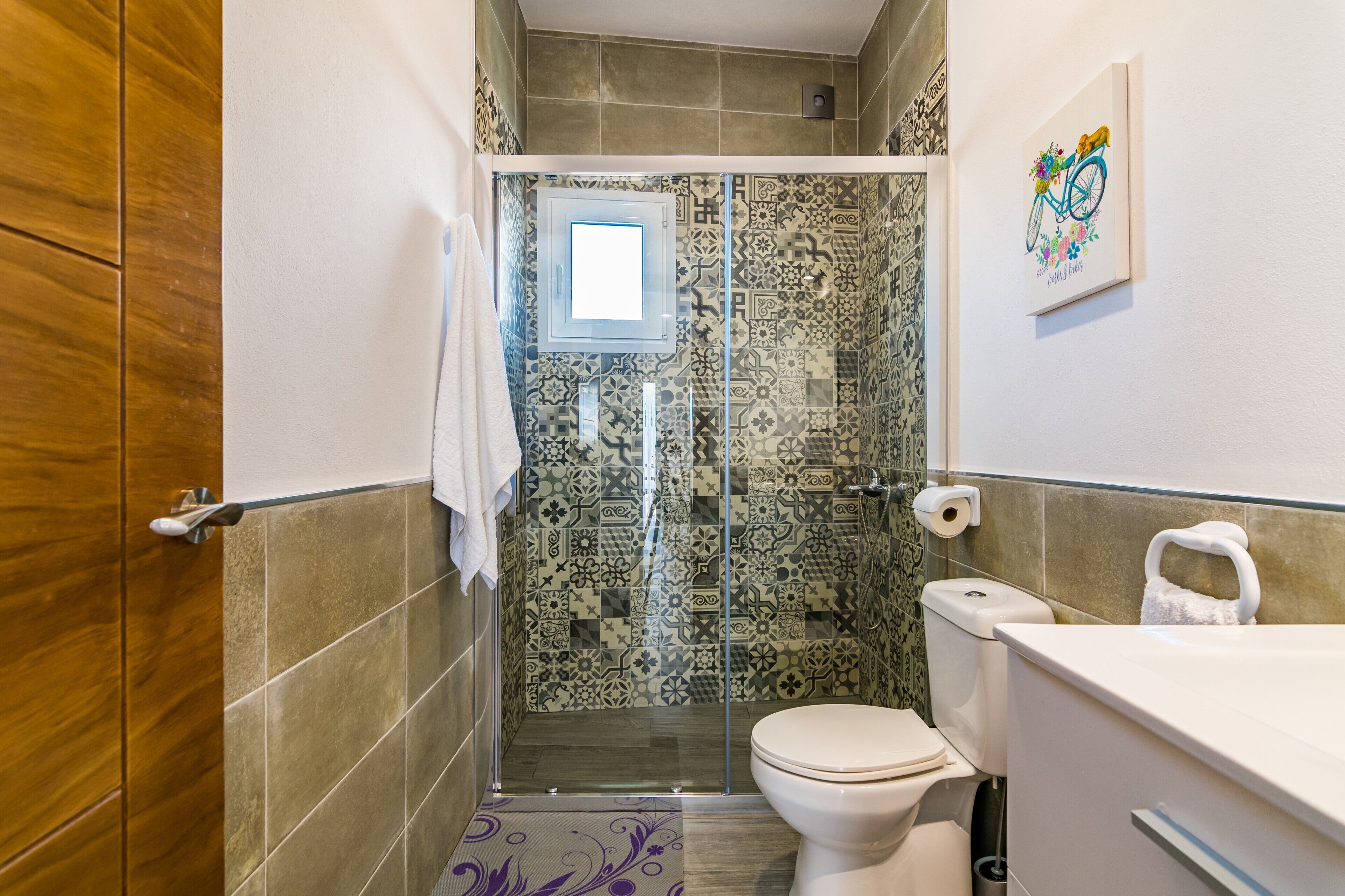 Une salle de bain équipée d’une douche, de toilettes et d’un lavabo, avec des carreaux décoratifs et une fenêtre.