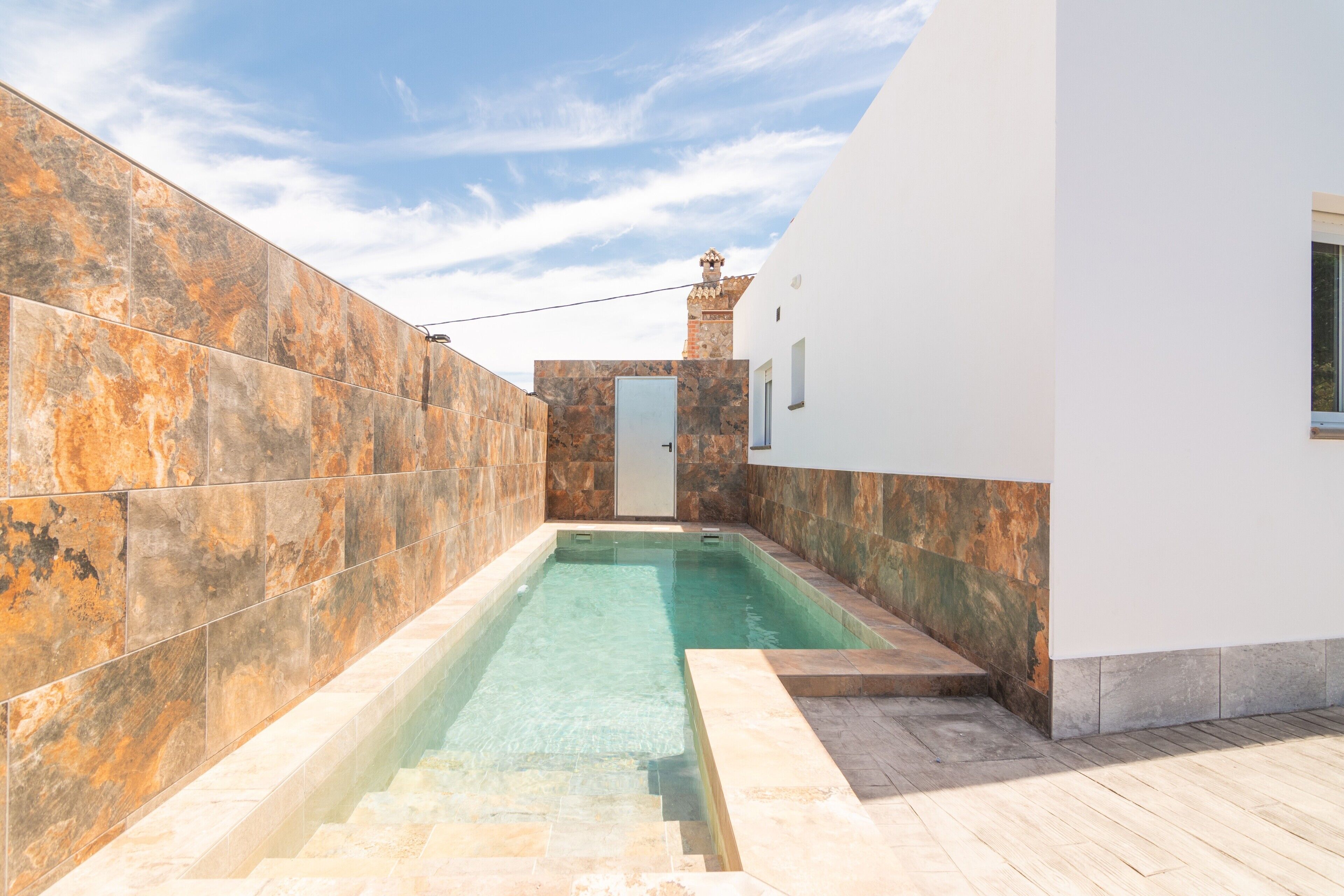 Une piscine avec un mur en pierre d’un côté et un bâtiment blanc de l’autre.