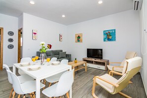 Una sala moderna con una mesa de comedor, sofá, televisor y decoración de pared con temática de cactus.