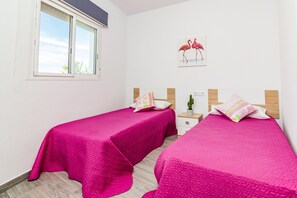 Una habitación con dos camas, una ventana, una mesita de noche, un cactus y un cuadro de flamencos.