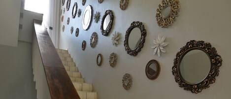 A staircase with a wooden handrail leading to a landing where multiple ornate mirrors are displayed on the wall.