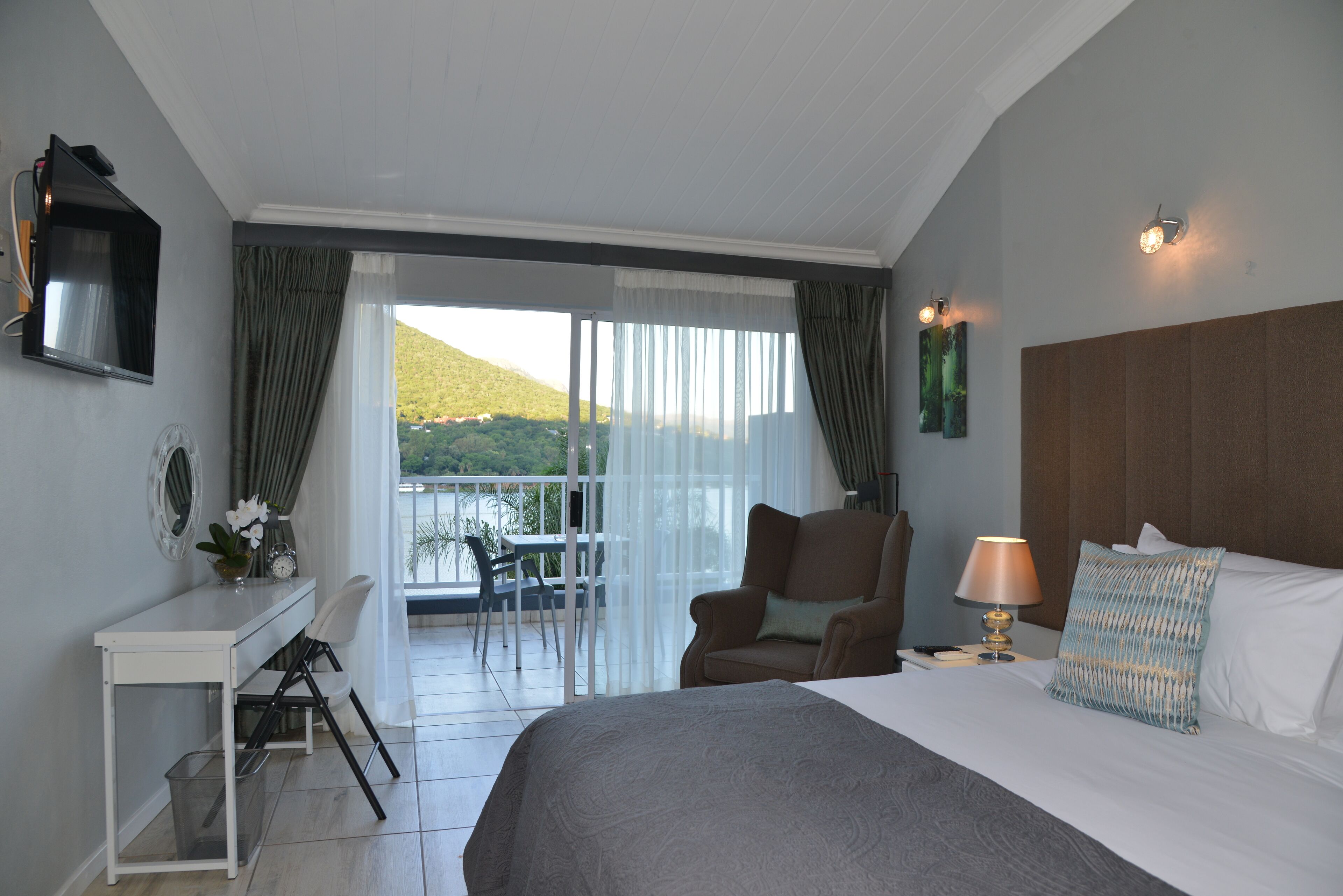 A hotel room with a bed, a desk with a chair, a TV, a lamp, and a view of the outdoors.