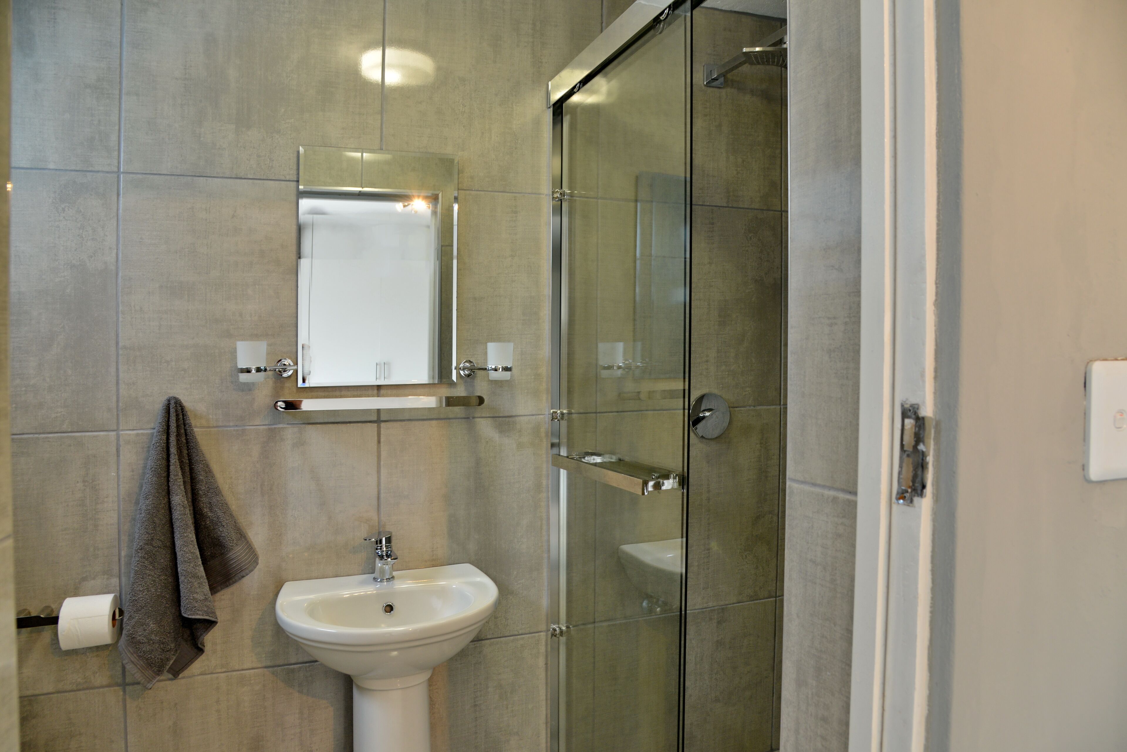 A bathroom with a glass shower enclosure, a pedestal sink, and a mirror above the sink.