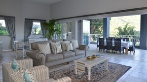 A spacious living area with a sofa, chairs, a dining table, and a balcony with a view of greenery. - The Shore House (Hartbeespoort)