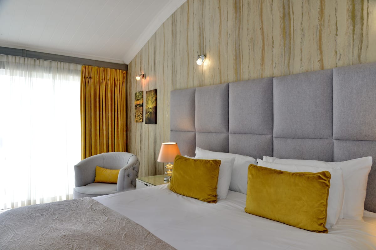 A hotel room with a large bed, a chair, a nightstand with a lamp, and a wall with a textured pattern.