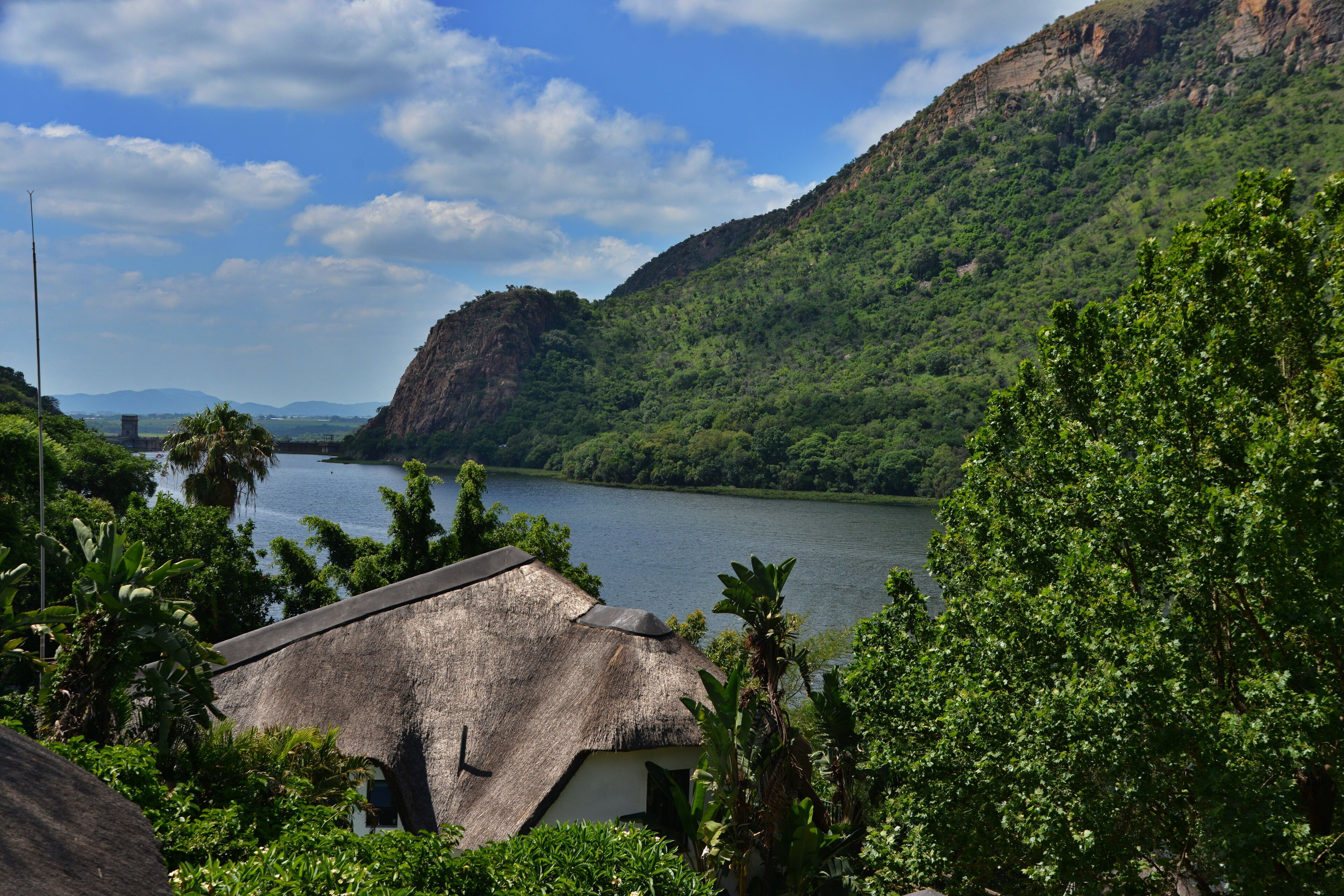 A thatched-roof building with a view of a river and mountains.