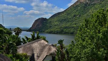 A thatched-roof building with a view of a river and mountains.